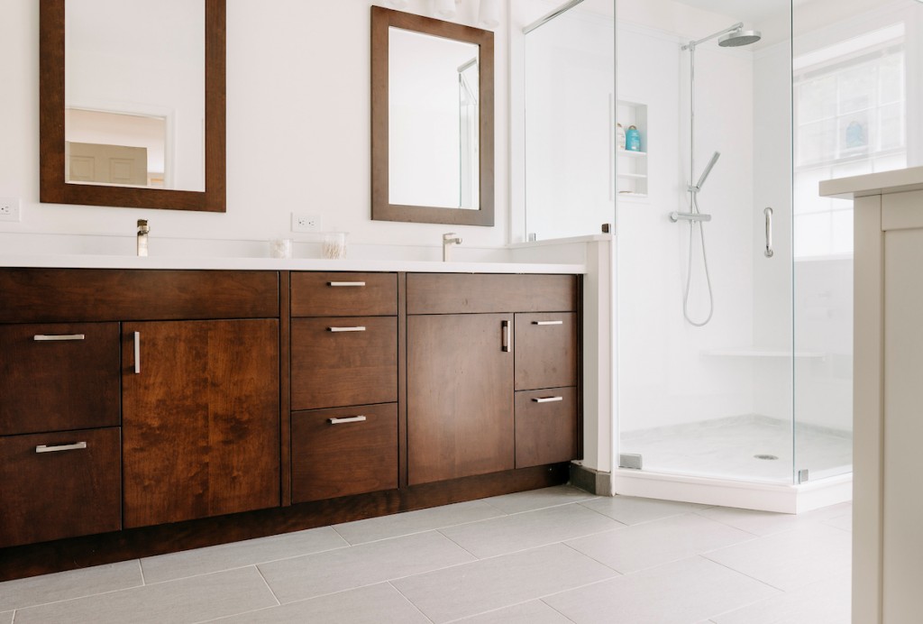 Frameless glass shower with rain head and handheld in Ardmore, PA bathroom remodel — Walnut Shaker double vanity, Corian countertops, glass shower