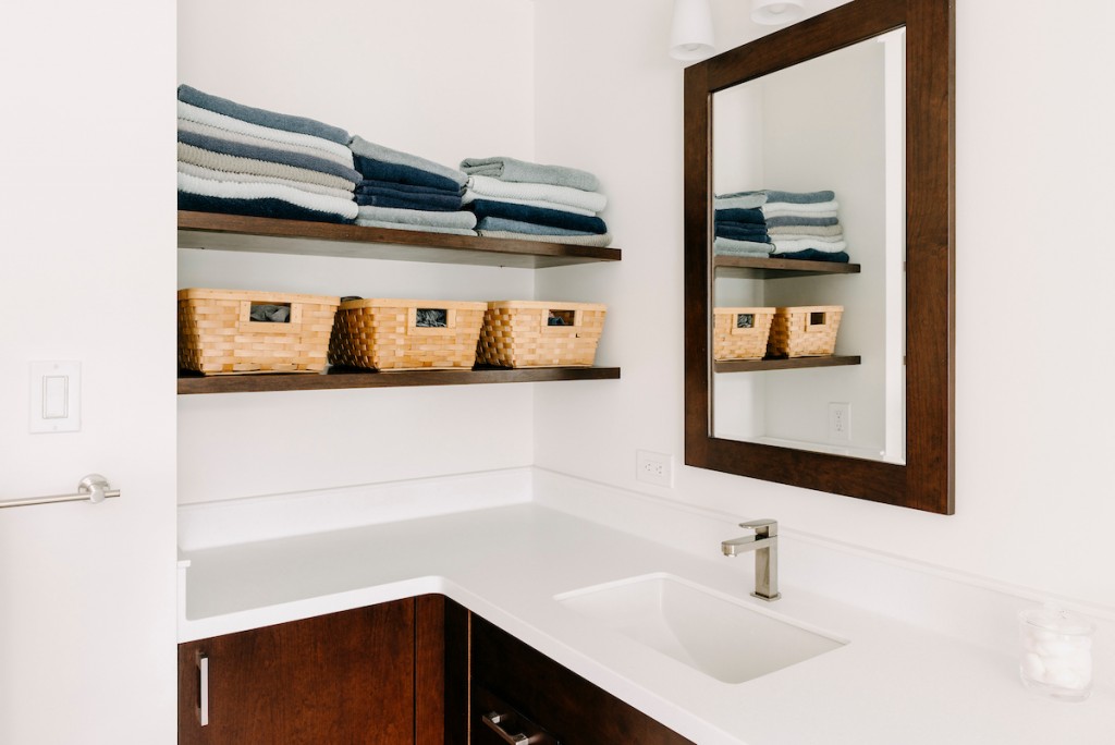 Long view of bathroom with walnut Shaker cabinetry in Ardmore, PA bathroom remodel — Walnut Shaker double vanity, Corian countertops, glass shower