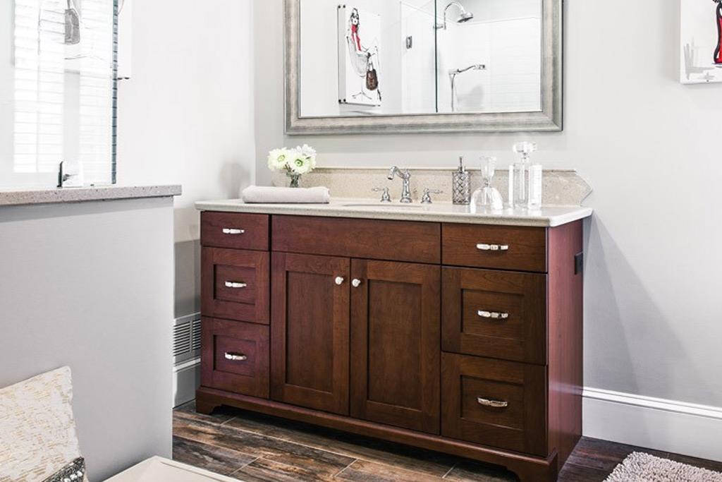 Chester Springs bathroom remodel vanity straight-on view — dark stained Shaker vanity with sandstone Corian counter, silver-leaf framed mirror, dark wood-look porcelain plank floor