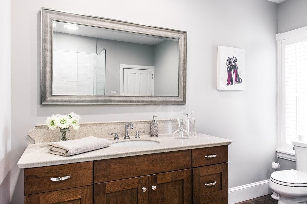 Chester Springs hall bathroom with seamless sandstone Corian counter and shower walls, stained frameless Shaker vanity, frameless half-wall walk-in shower, and dark wood-look porcelain plank floors in Chester Springs, PA — bathroom remodel by Fedor Fabrication