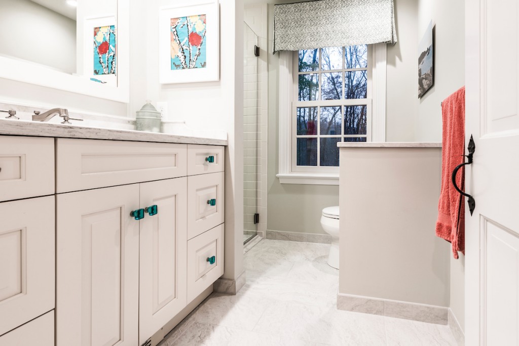 Downingtown bathroom remodel wide view — cream raised-panel vanity with turquoise glass pulls, marble counter, frameless walk-in shower beyond, half-wall divider with toilet alcove