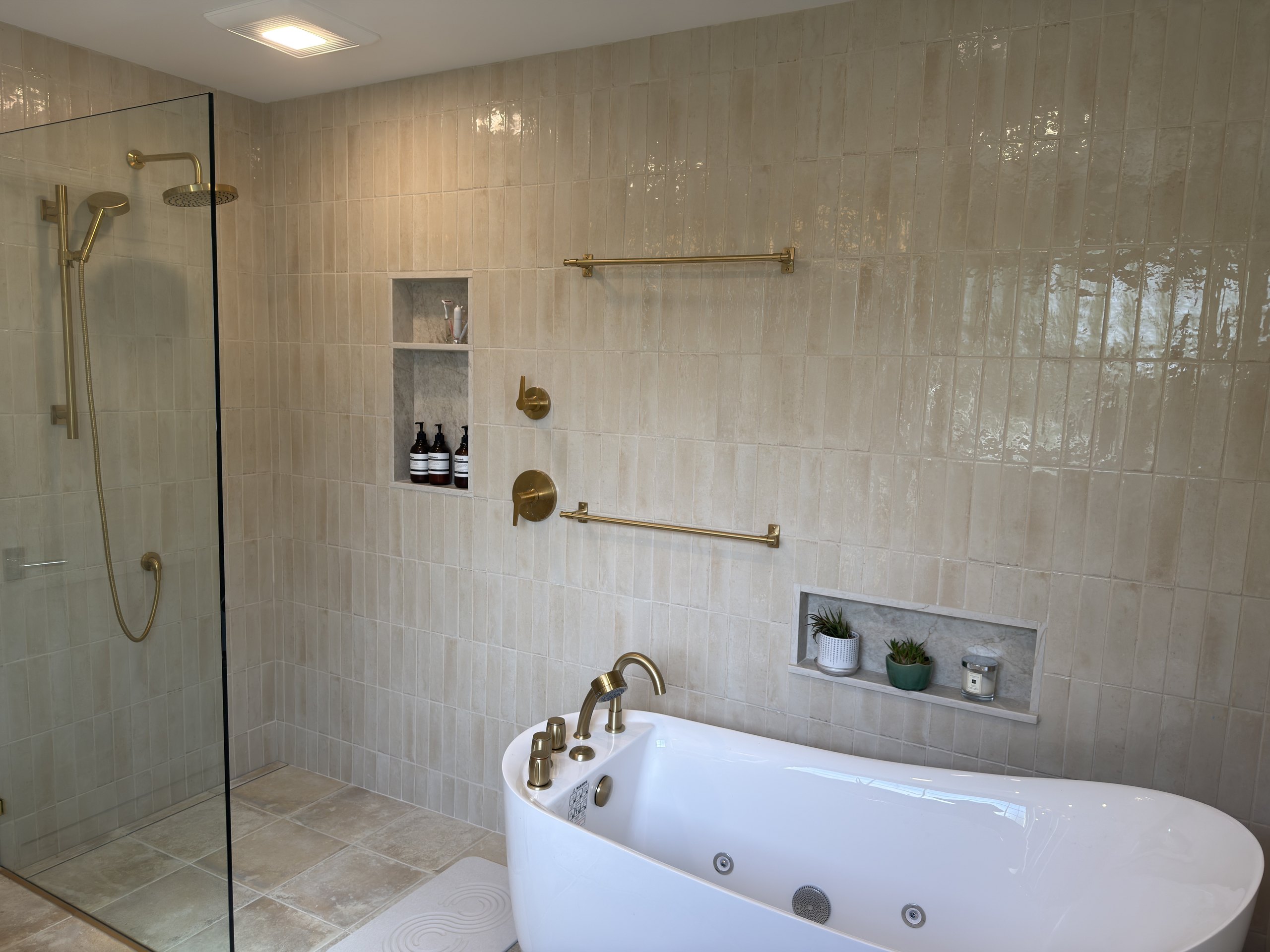 Malvern primary bathroom with a frameless glass walk-in shower, freestanding soaking tub, and brass fixtures on glossy cream Look Lino tile