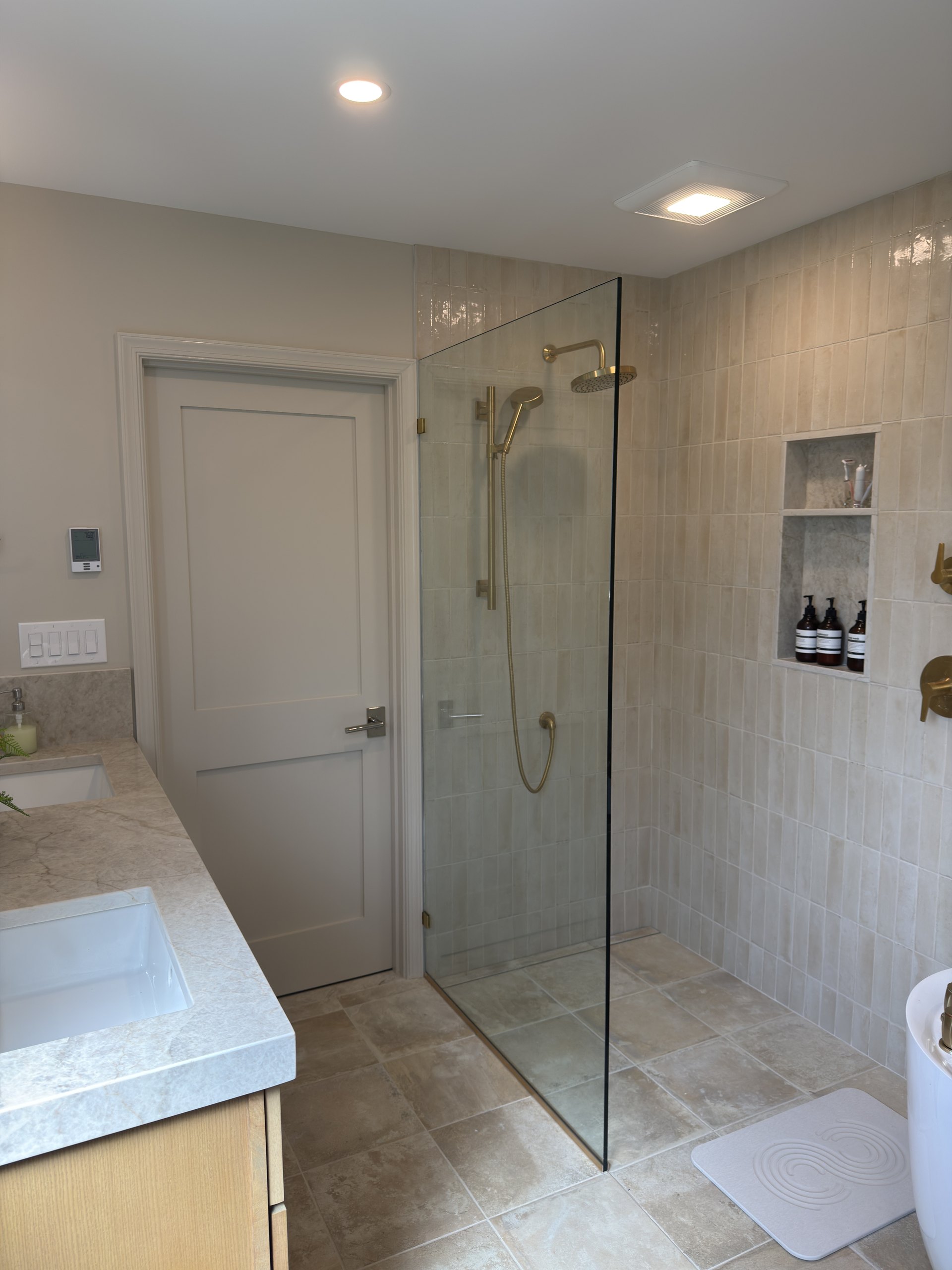 Frameless glass walk-in shower with brass trim and a quartz-framed niche next to the freestanding tub