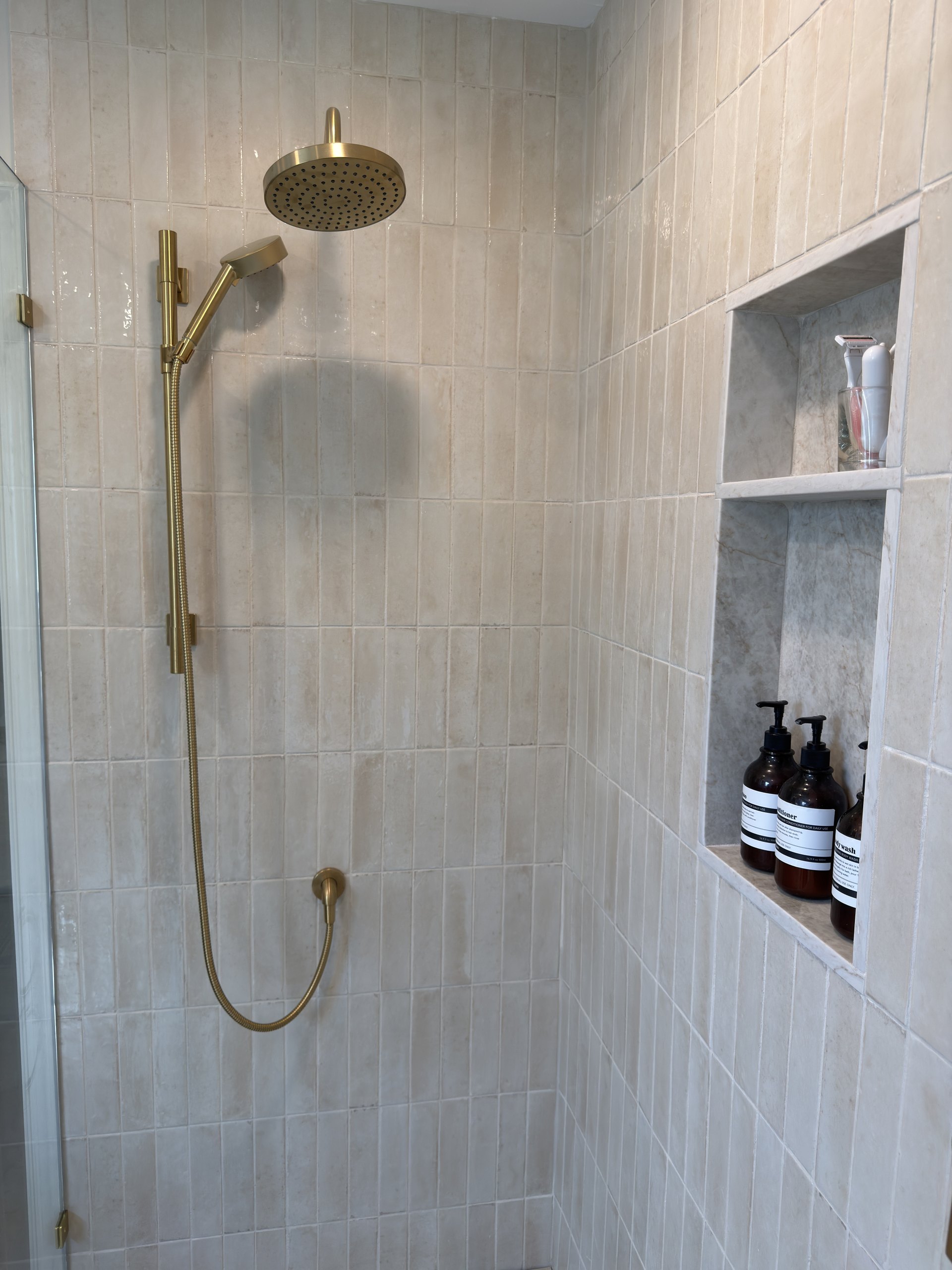 Brass shower head and handheld on a slide bar against glossy cream Look Lino wall tile
