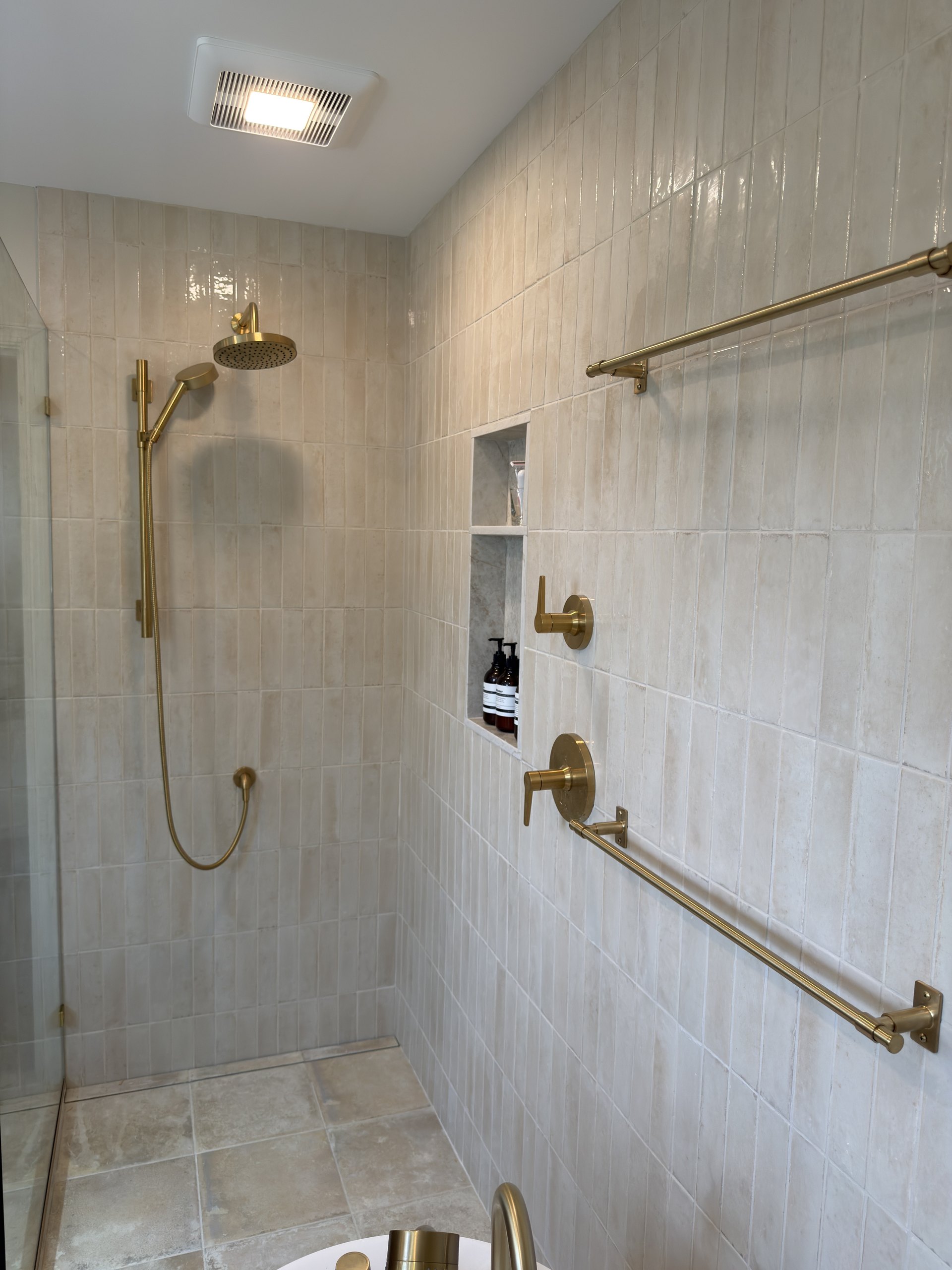 Walk-in shower wall with brass towel bars, quartz-framed niche, and stacked cream tile