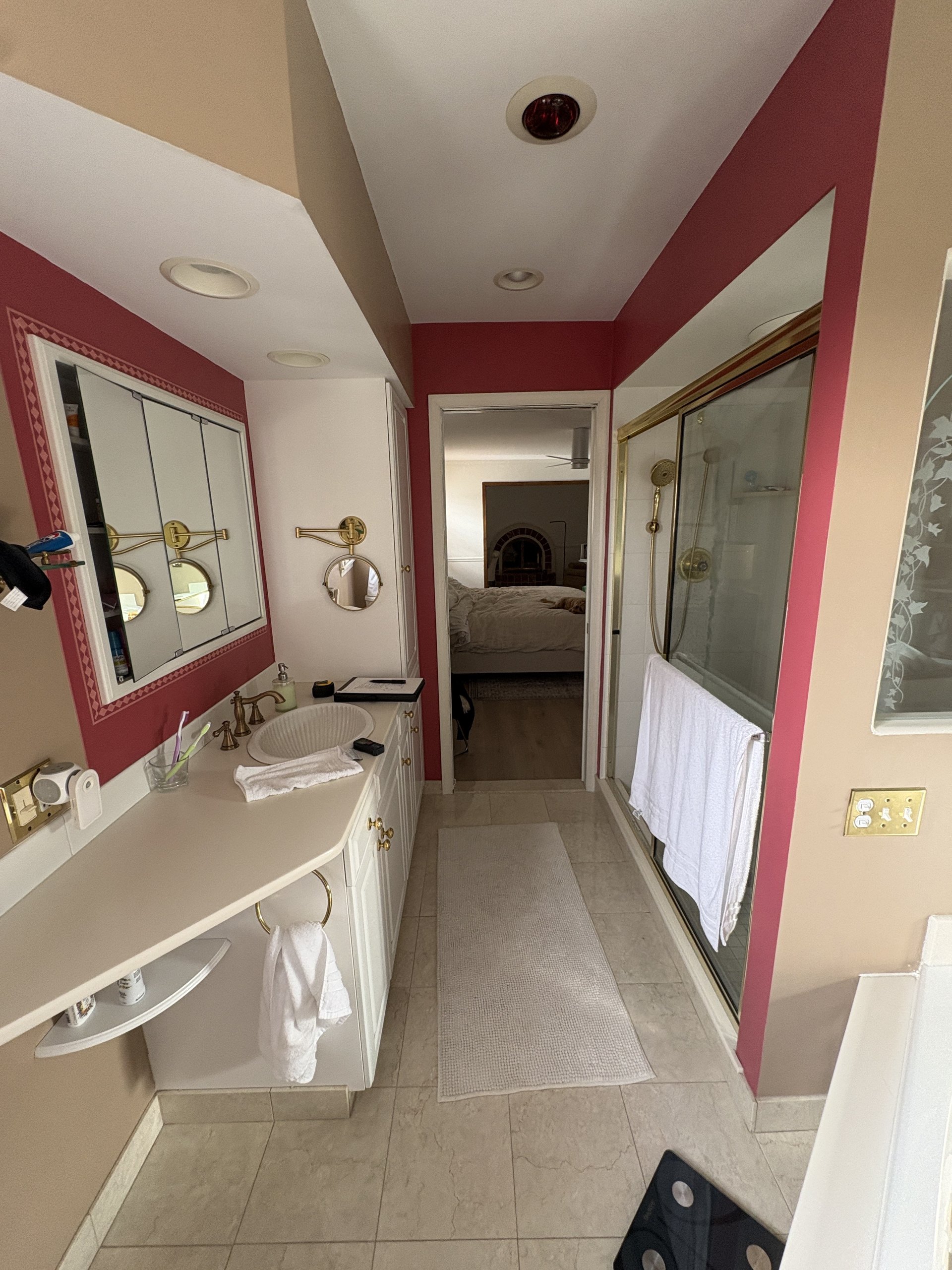 Original 1990s primary bath with mauve walls, gold-framed mirror, and a corner glass-and-brass shower