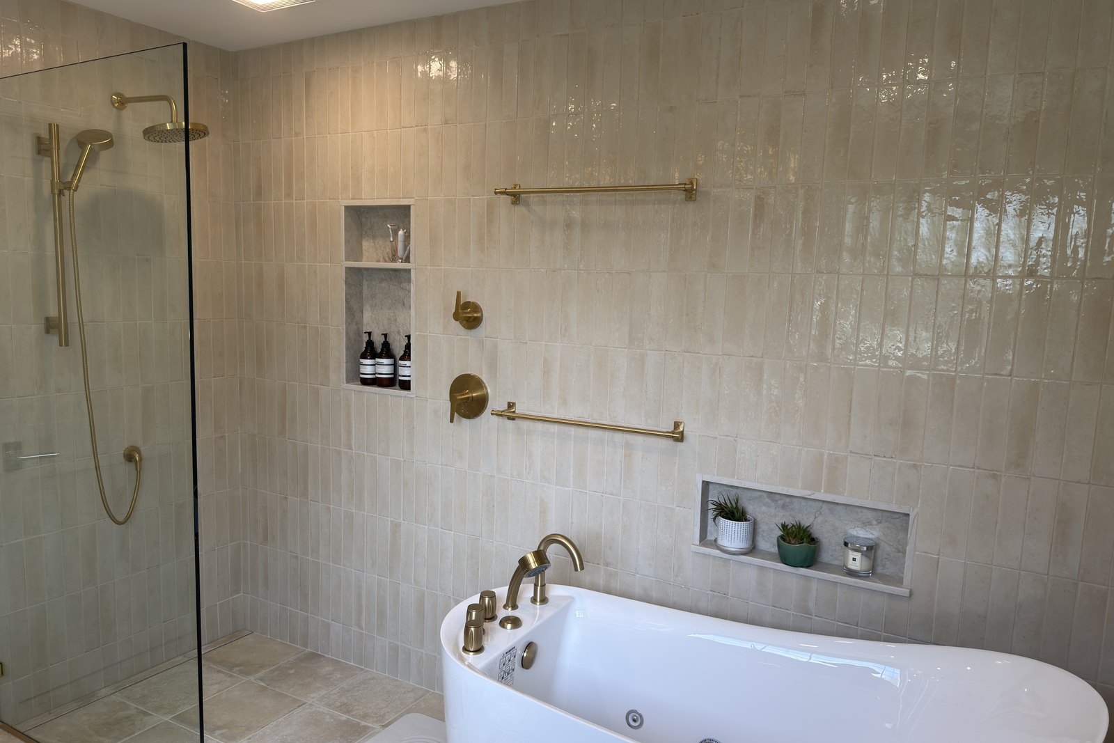 Malvern primary bathroom with a frameless glass walk-in shower, freestanding soaking tub, and brass fixtures on cream Look Lino tile, bathroom remodel by Fedor Fabrication