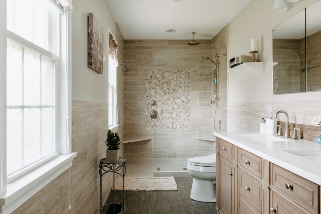 Curbless walk-in shower with travertine plank tile in Newtown Square, PA bathroom remodel — Cerused oak raised-panel double vanity