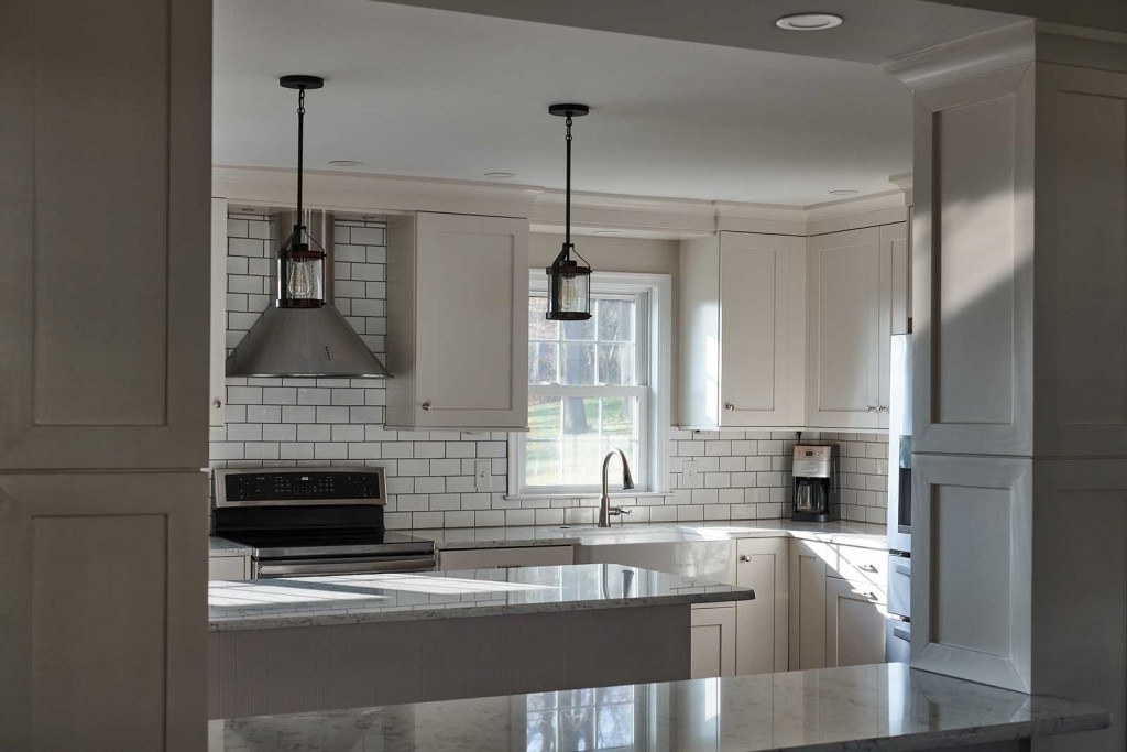 Villanova kitchen range wall with stainless chimney hood, two black caged-lantern pendants, and dark-grout subway tile backsplash