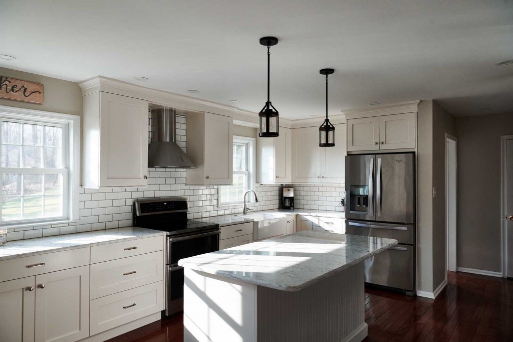 Peninsula-to-island kitchen rebuild with white Shaker frameless cabinets, quartz counters, classic subway tile in dark grout, and a beadboard-back island in Villanova, PA — kitchen remodel by Fedor Fabrication