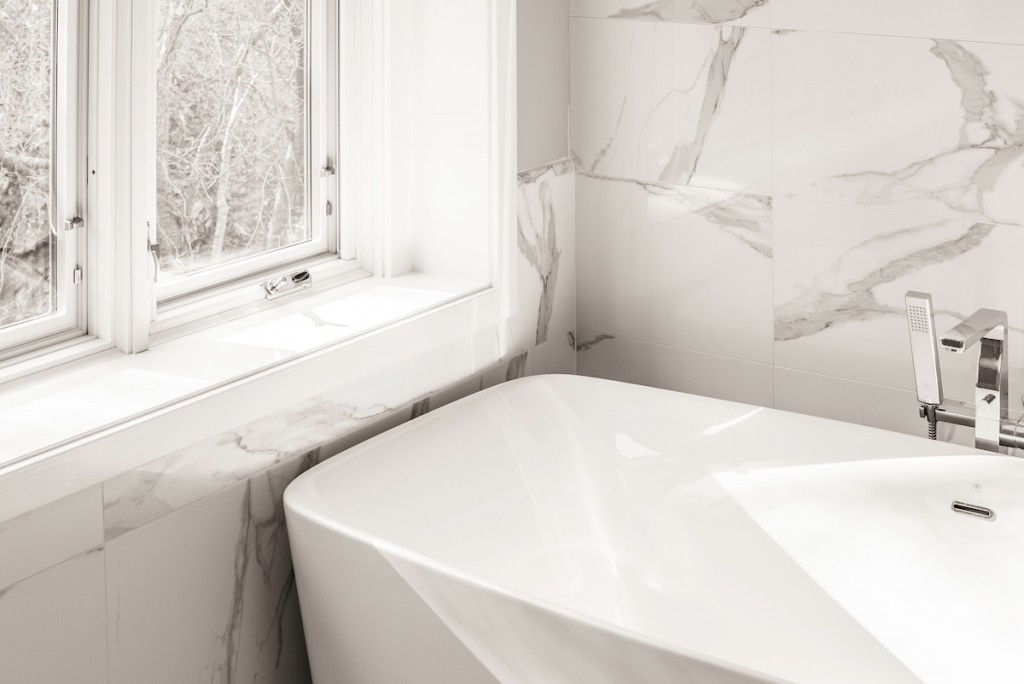 Soaker tub at casement window with porcelain surround in Wayne, PA bathroom remodel — Quiet luxury master bath in Calacatta-look large-slab porcelain