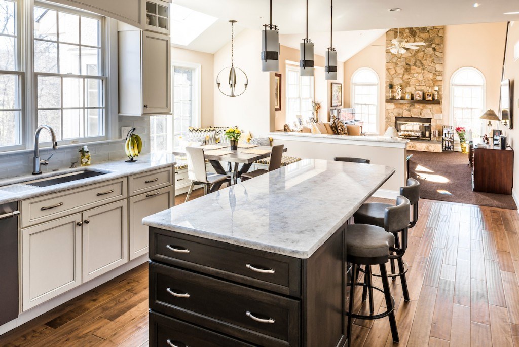 Wayne kitchen sink wall — undermount stainless sink under the window, cabinetry valance, hand-scraped hardwood floor, stone fireplace beyond
