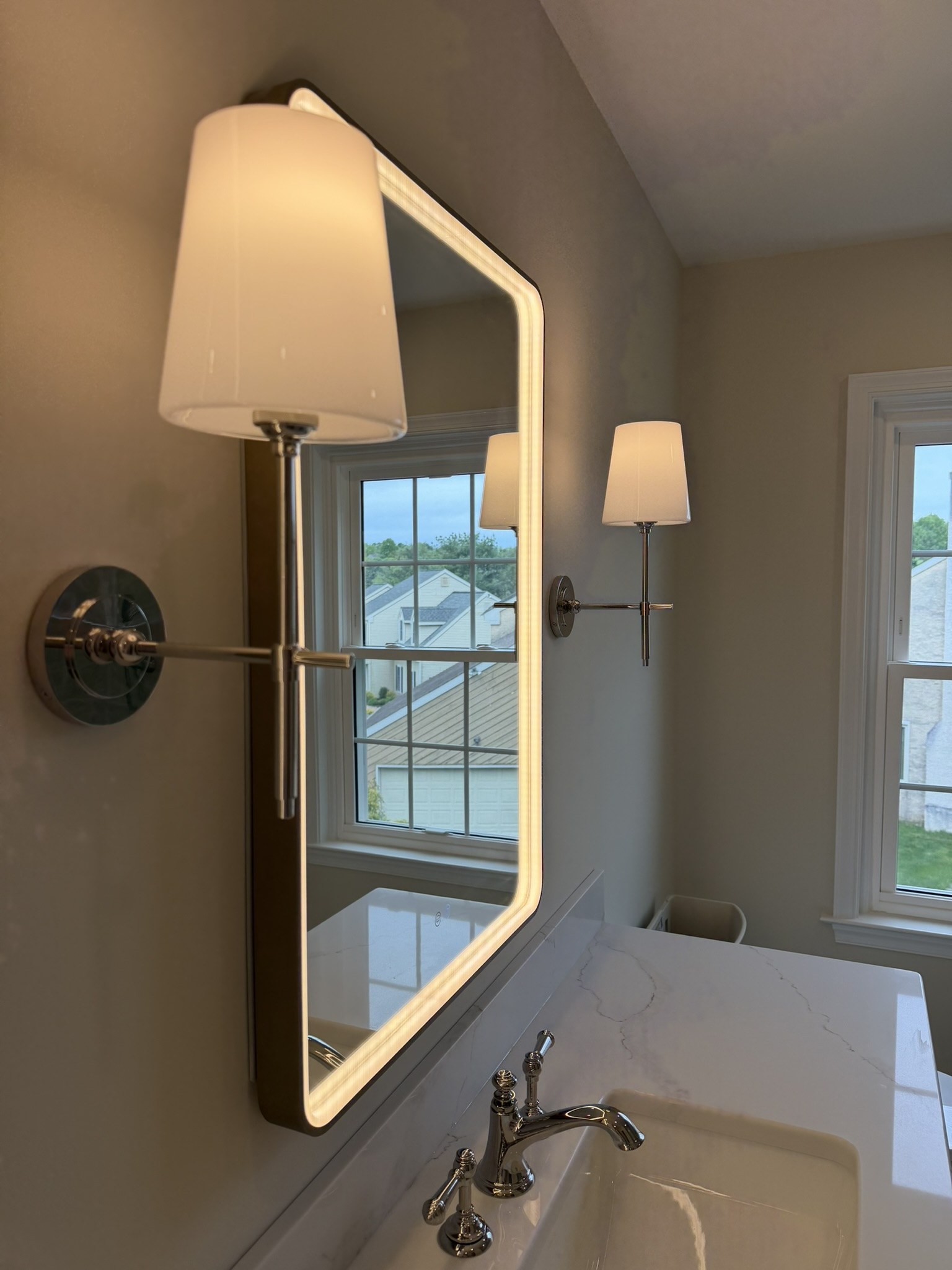 Slim polished nickel wall sconce with white frosted glass shade beside an LED medicine cabinet mirror