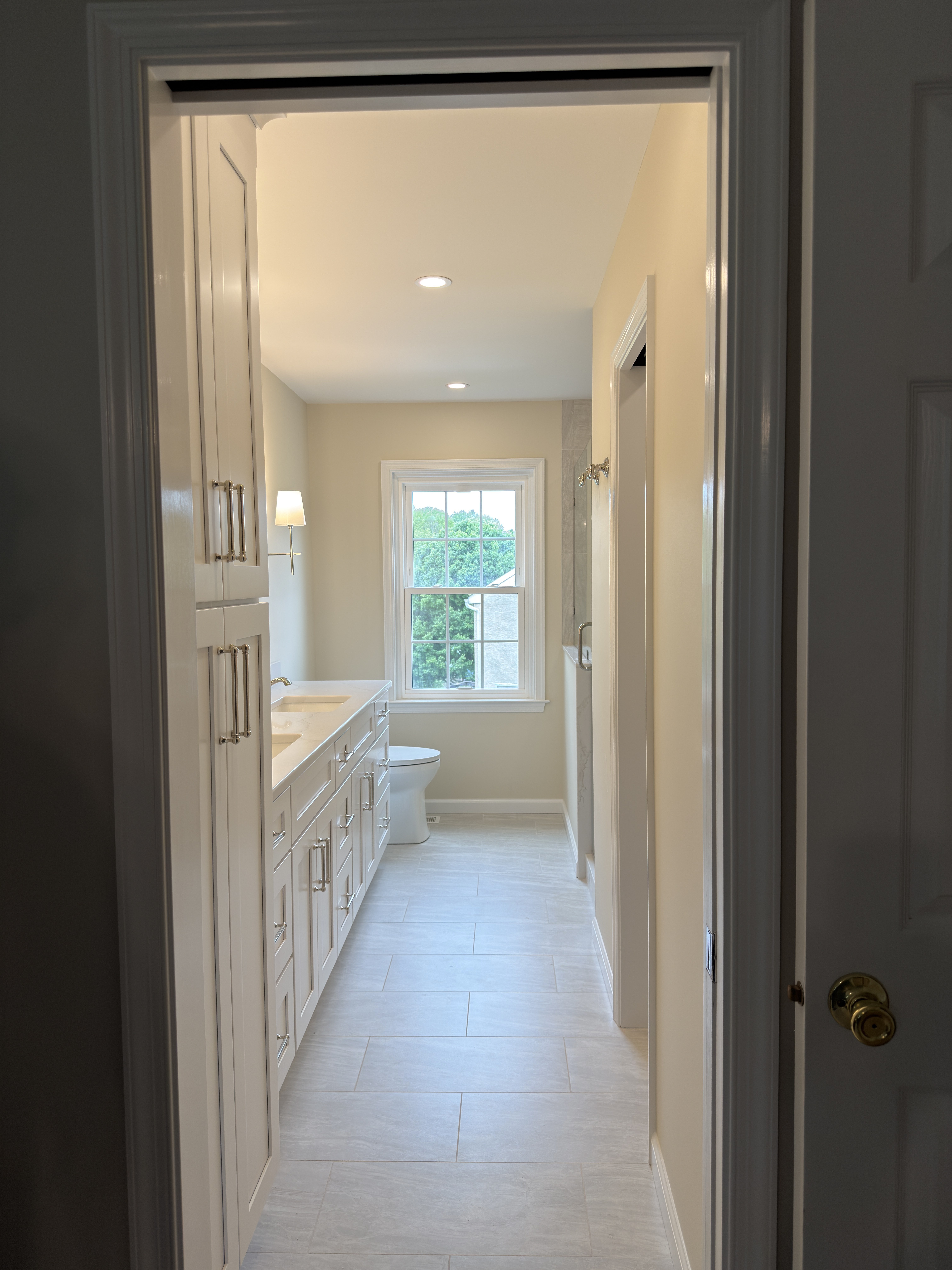 View through the bedroom pocket door into the Wayne primary bathroom toward the window and double vanity
