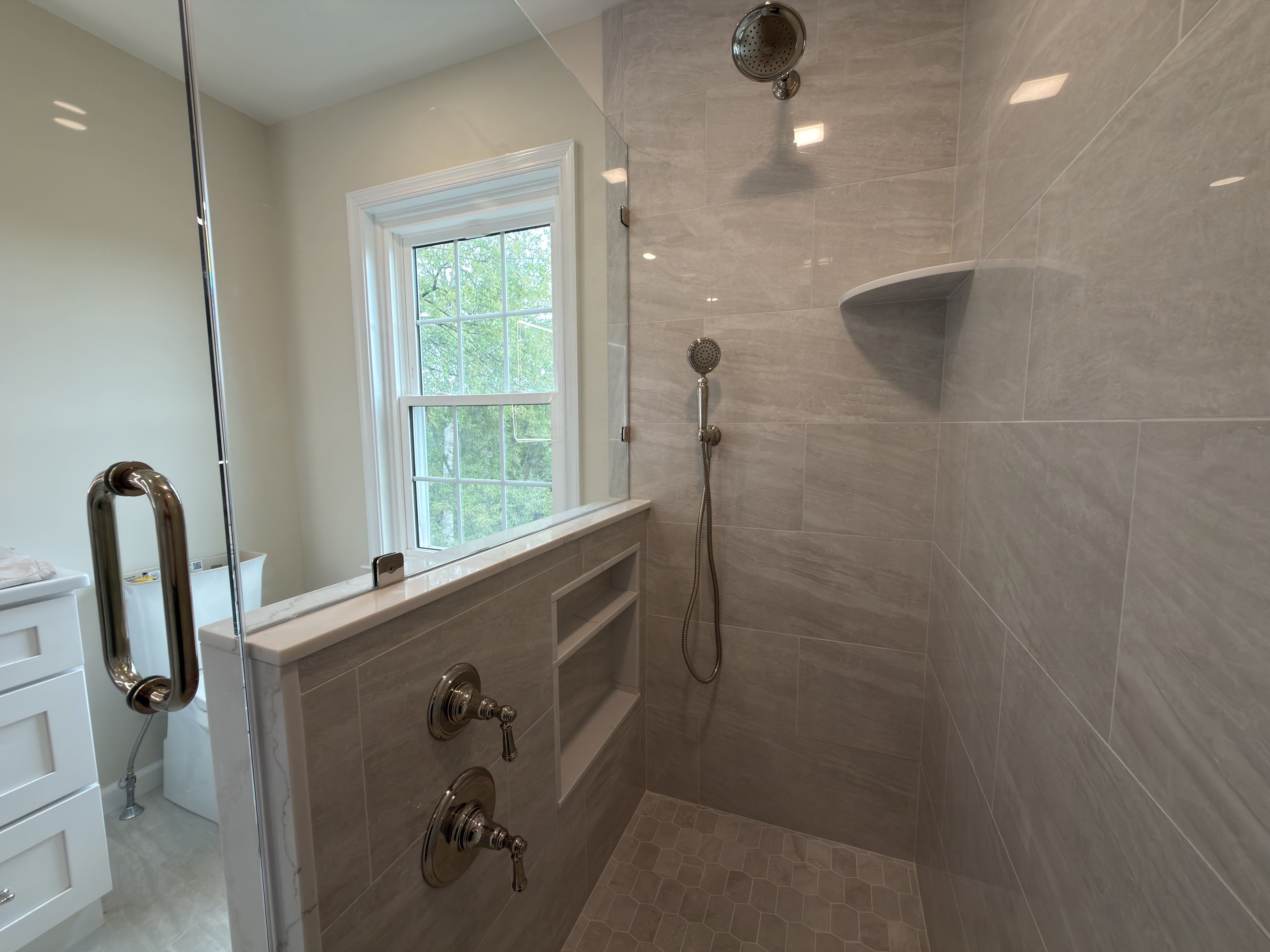Shower interior with light through a window, polished nickel rain head and handheld, and a built-in niche