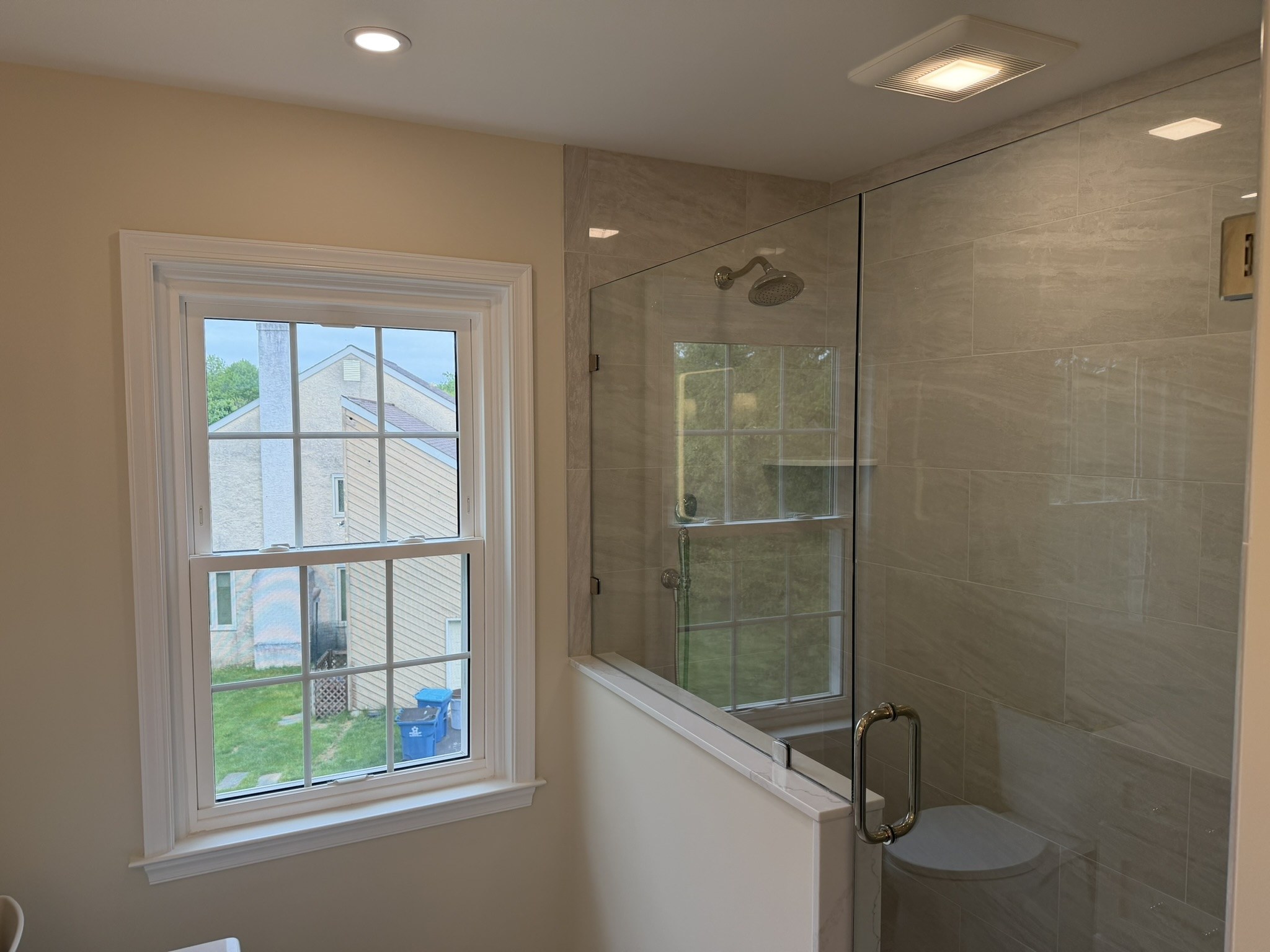Wide view of the Wayne primary bathroom from the doorway showing shower, half-knee wall, and natural light from the window