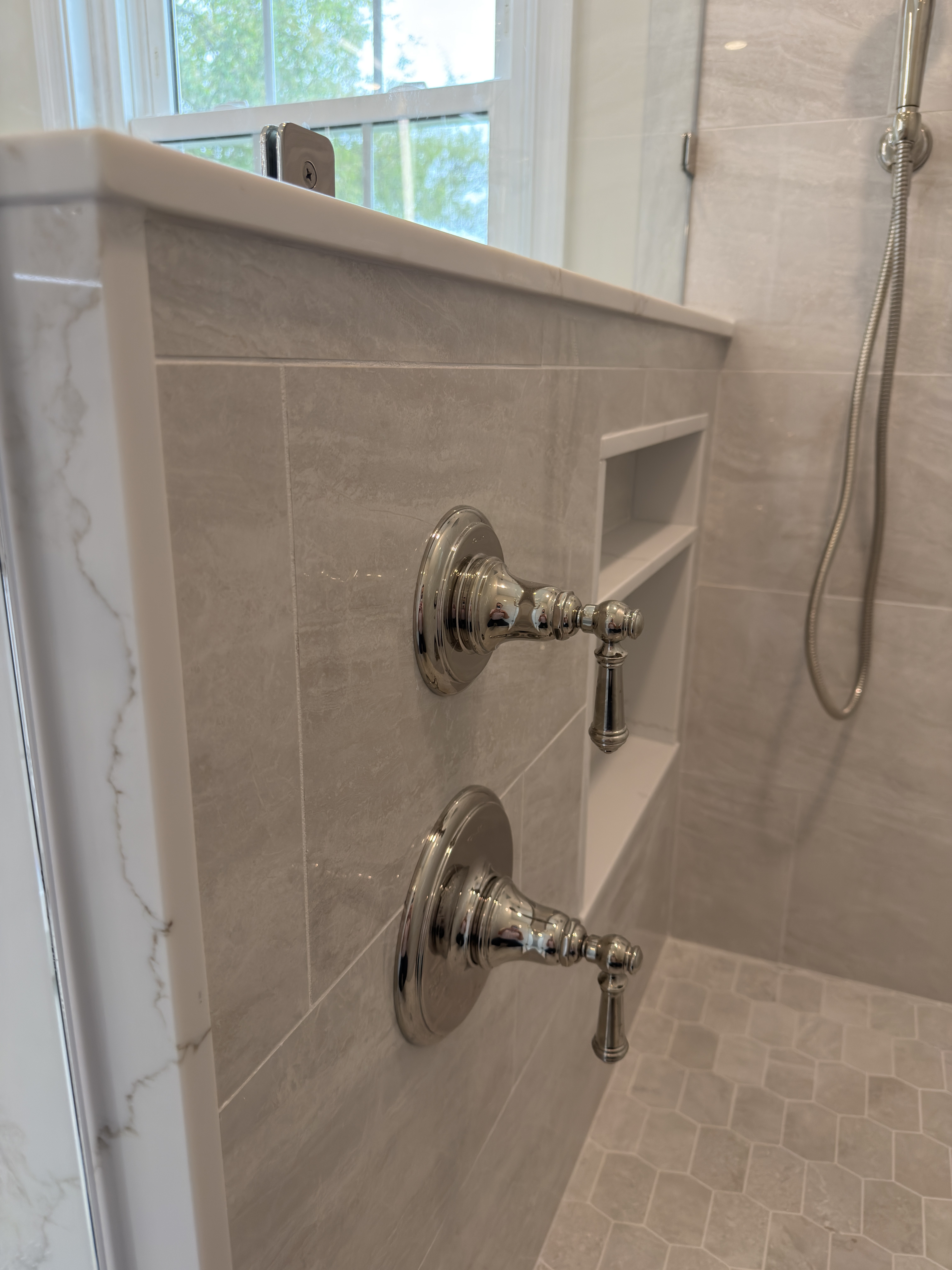 Polished nickel shower controls close-up next to the quartz-capped half-knee wall with gold veining