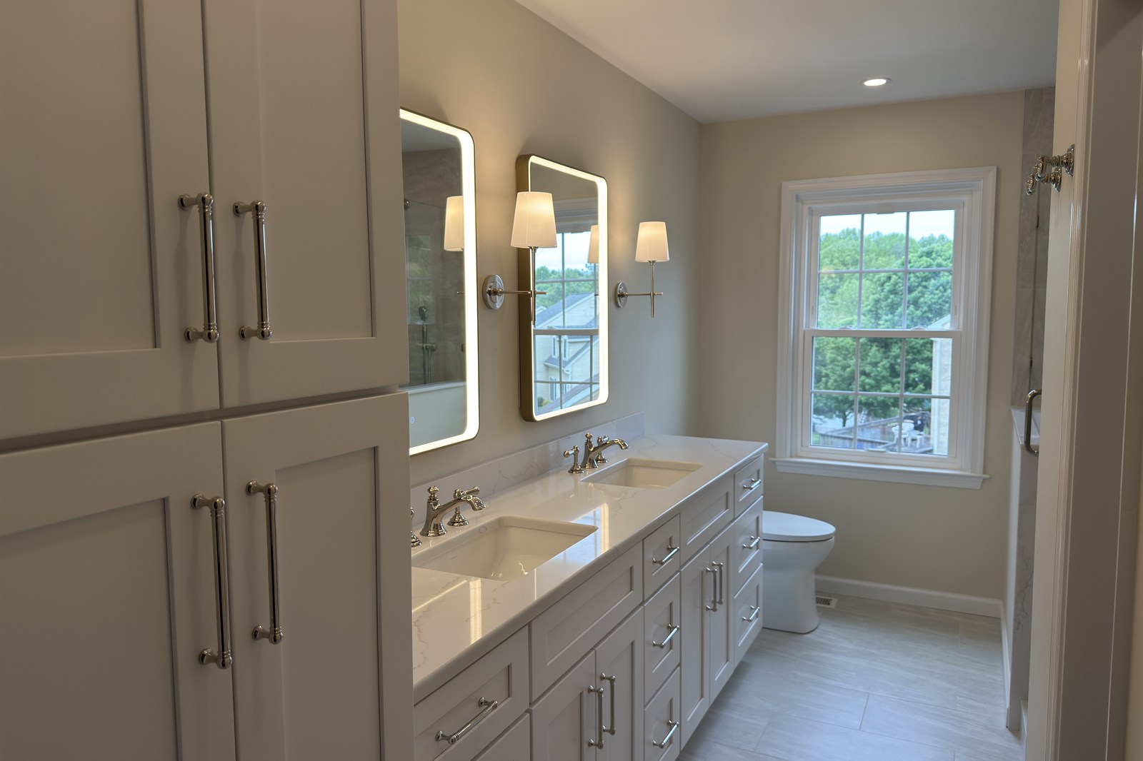 White Shaker double vanity with tall storage cabinet, polished nickel hardware, and LED mirrors in Wayne, PA — bathroom remodel by Fedor Fabrication