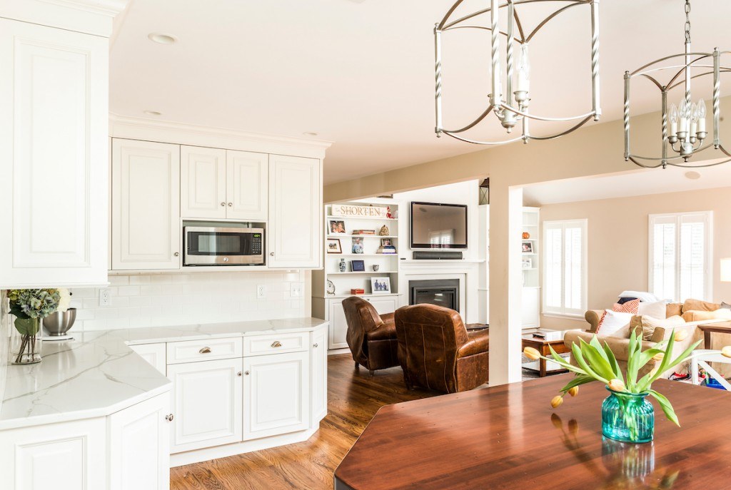 Wayne kitchen open to family room with white painted fireplace, flanking built-ins, and twist-frame lantern pendants over the butcher-block island