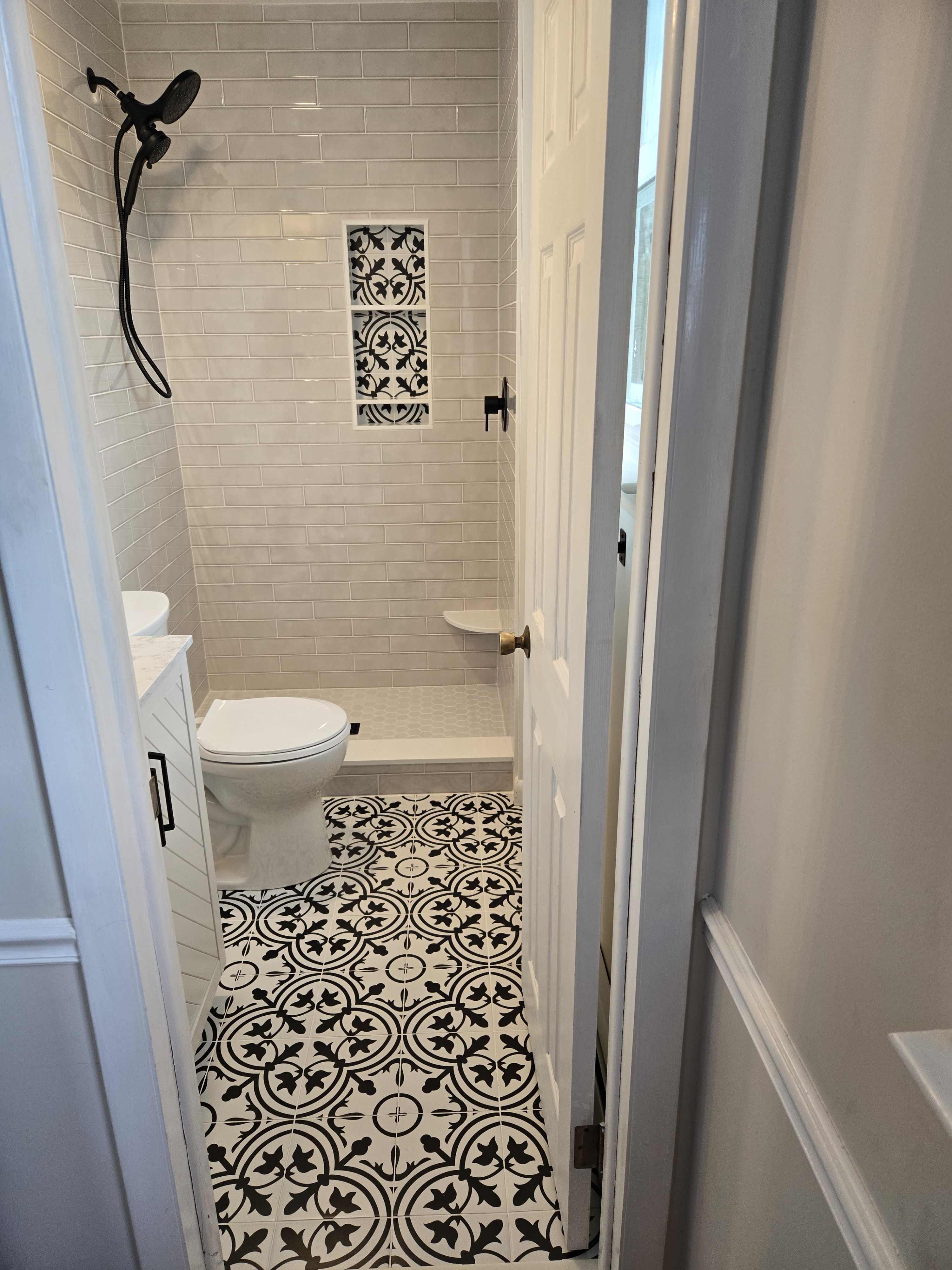 Small West Chester primary bathroom with black-and-white decorative floor tile, white subway tile shower, decorative niche, and matte black fixtures — bathroom remodel by Fedor Fabrication
