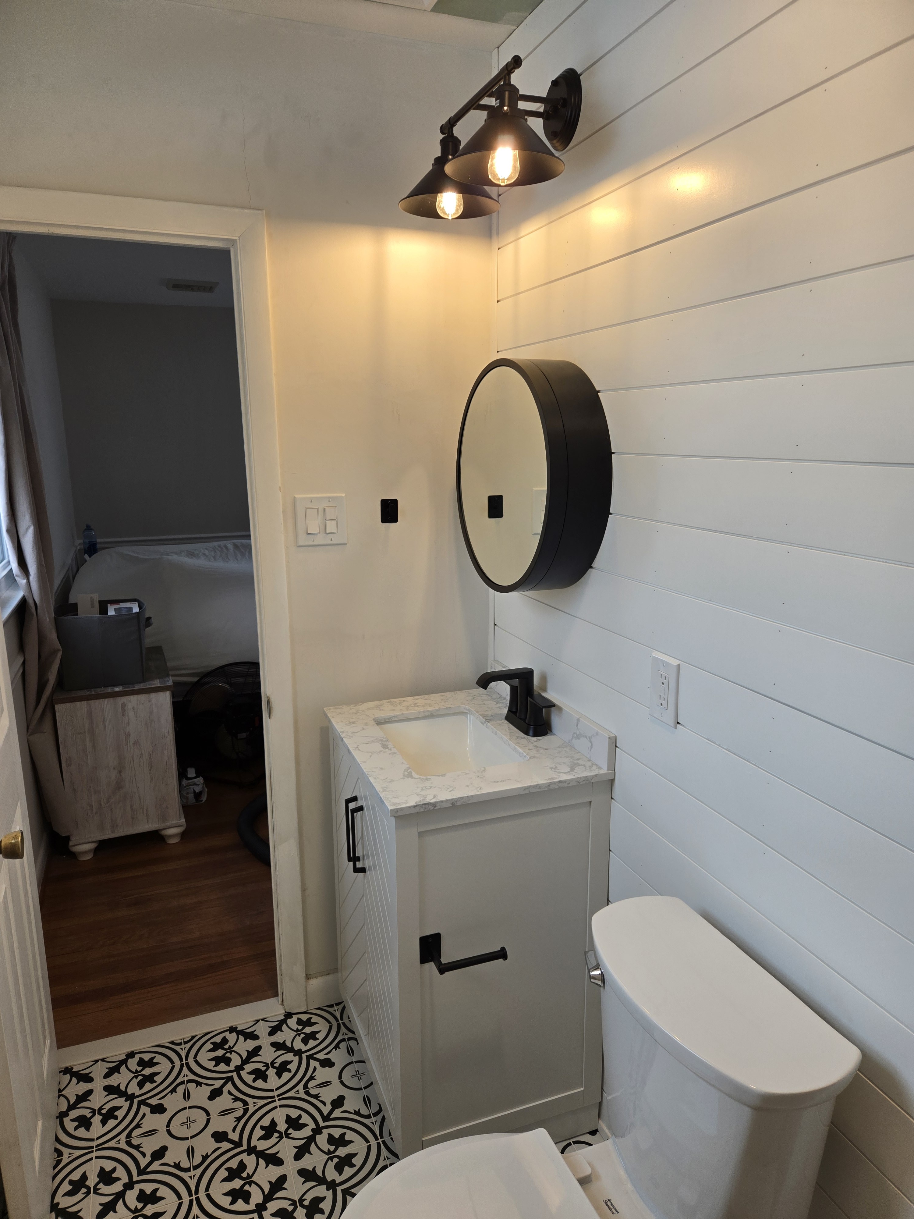 Vanity wall: white painted vanity with marble-look quartz, round matte black mirror, white horizontal shiplap, twin-bulb sconce — West Chester primary bathroom