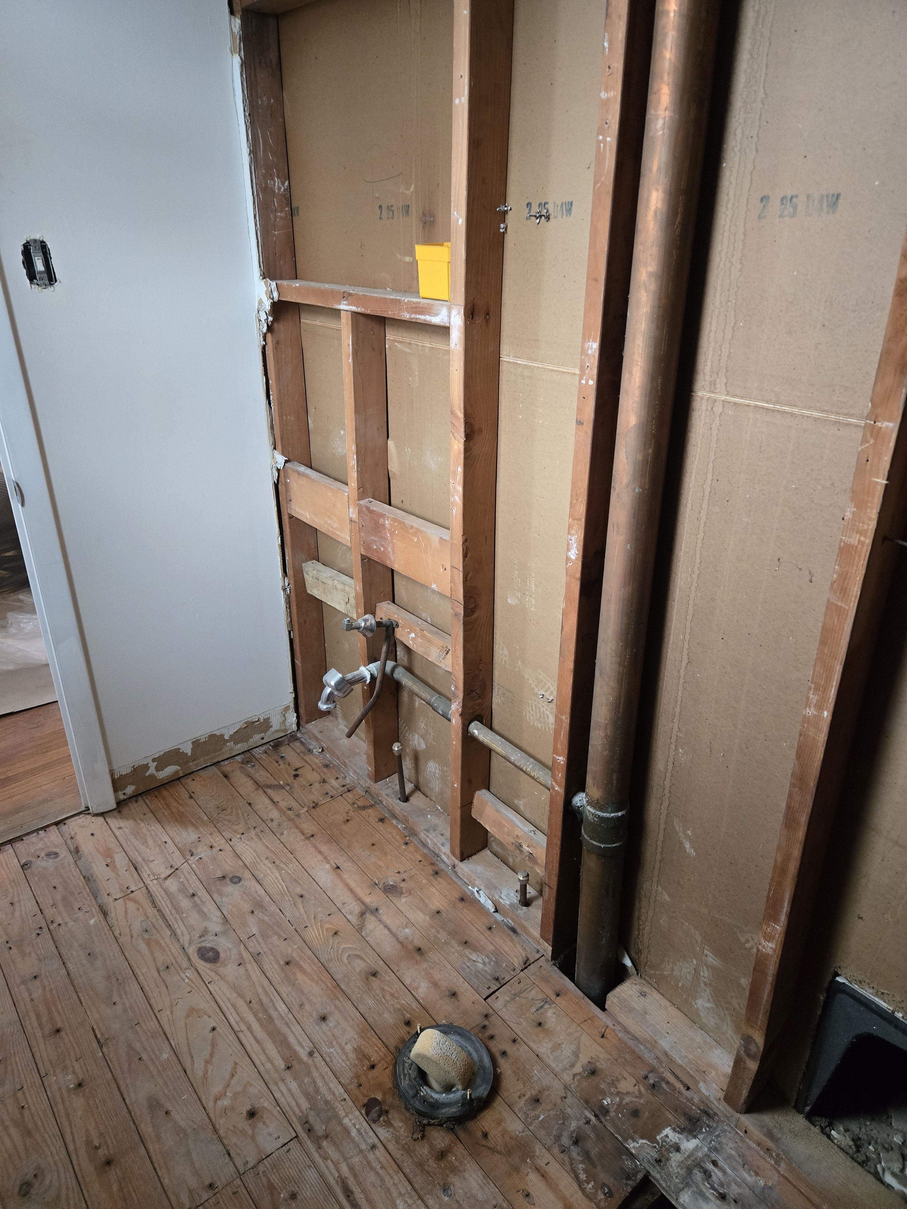 Plumbing rough-in — drain stack and supply lines visible, framing exposed, ready for Schluter waterproofing