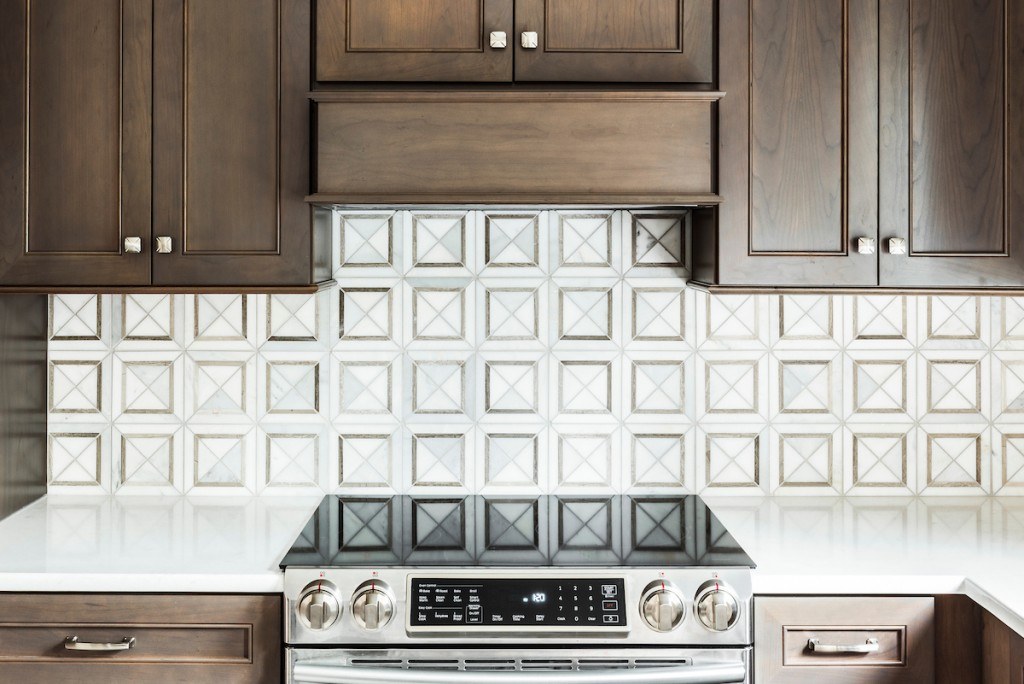 West Chester walnut kitchen detail showing 3D pyramid-cut marble mosaic backsplash and stained recessed-panel cabinets framing the range