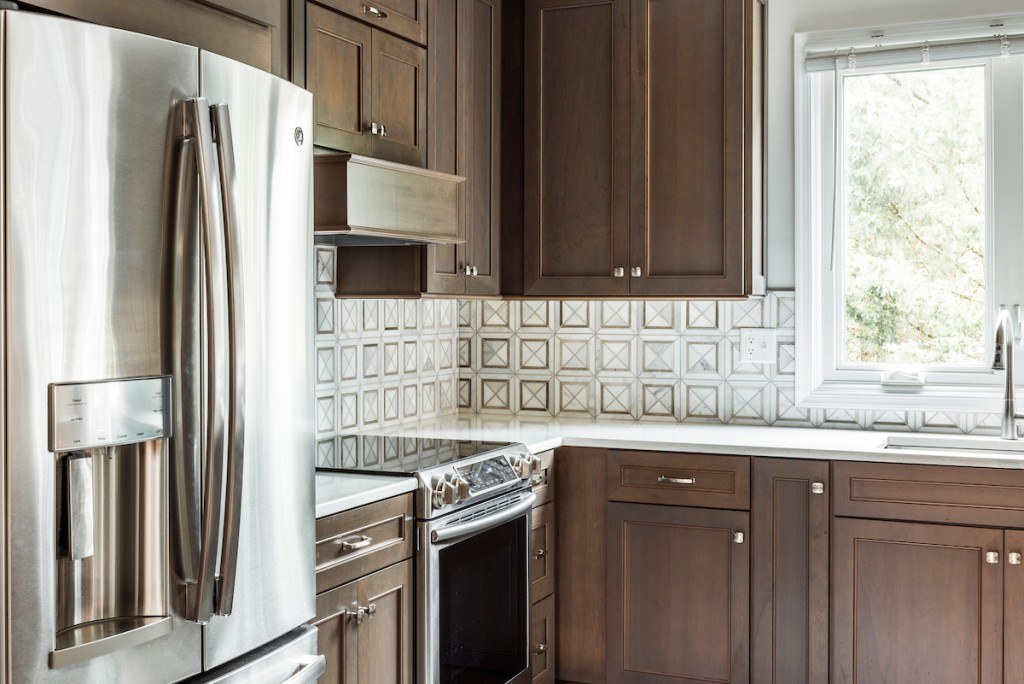 West Chester kitchen range wall — stainless slide-in range, GE Profile fridge, sculpted marble backsplash, and stained walnut frameless cabinets