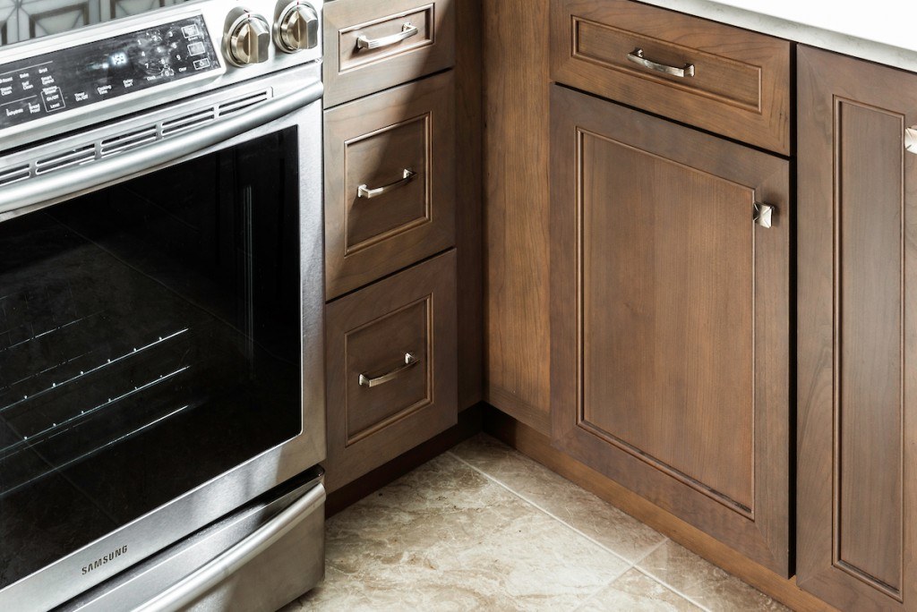 West Chester walnut kitchen detail of the sink wall — stained recessed-panel doors, white quartz counter, and 3D marble backsplash
