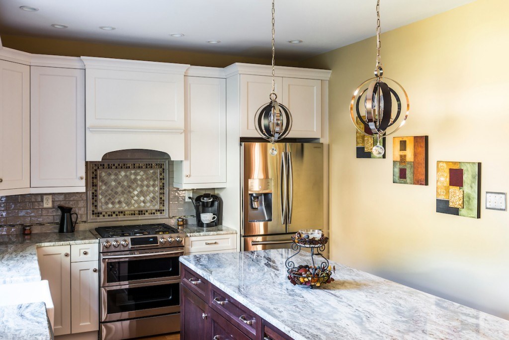 West Chester kitchen range wall with glass-fronted uppers, arched-corbel hood, and dark glass-mosaic-bordered mosaic centerpiece