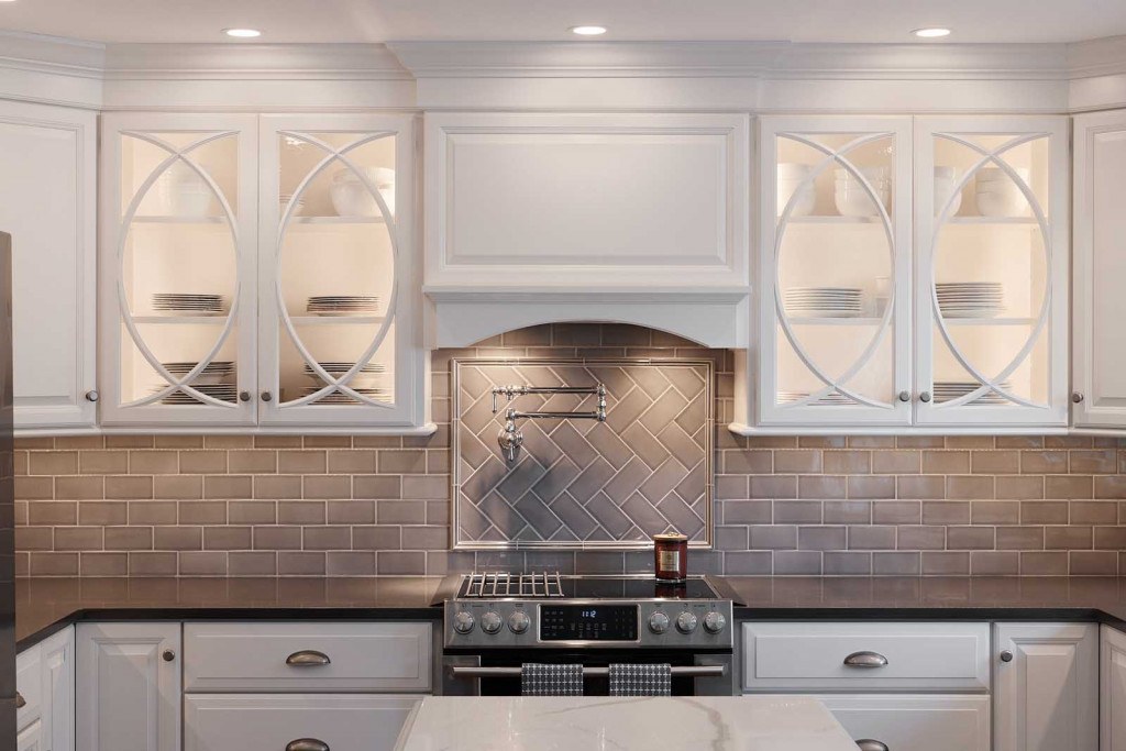 West Chester twist-on-white kitchen showing half-circle mullion glass uppers flanking the custom range hood with herringbone metal accent behind