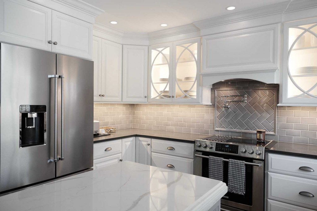 West Chester twist-on-white kitchen tight view of the half-circle mullion uppers, fridge, and herringbone metal accent backsplash