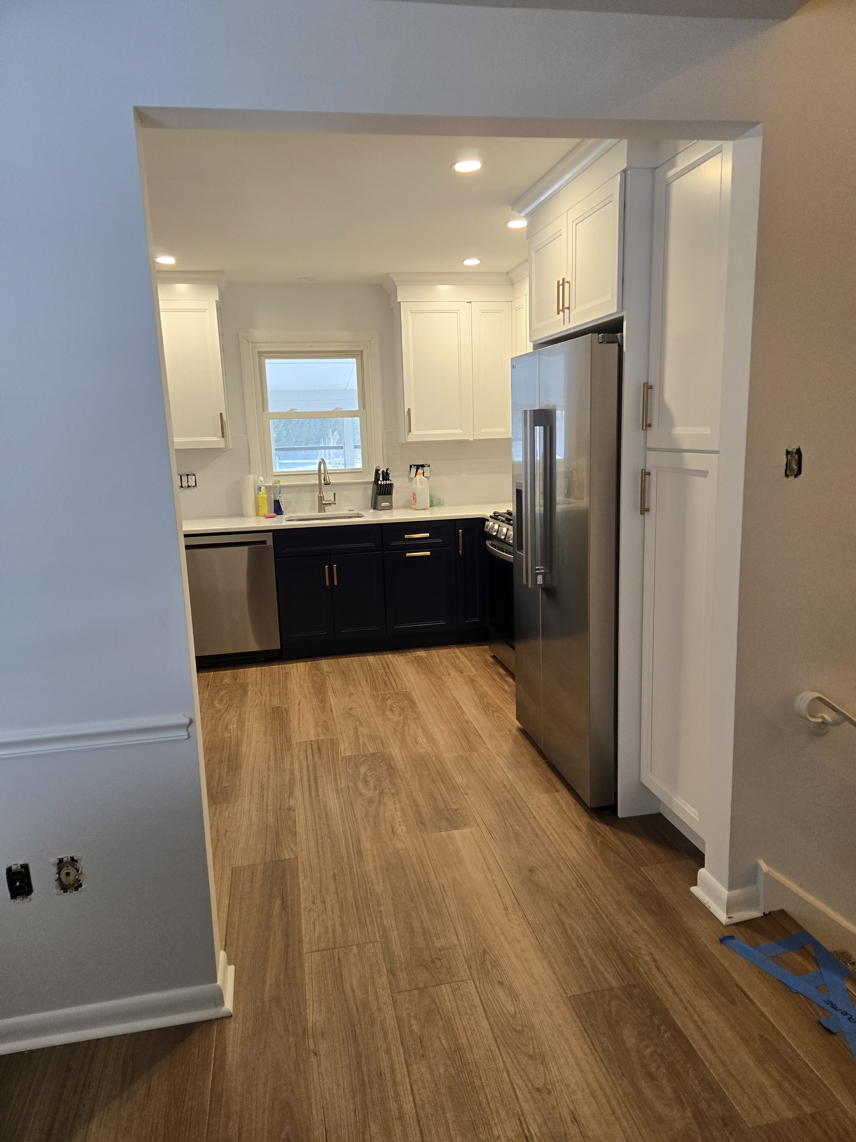 View through the widened doorway showing sink wall, navy island, and stainless side-by-side fridge — West Chester kitchen remodel