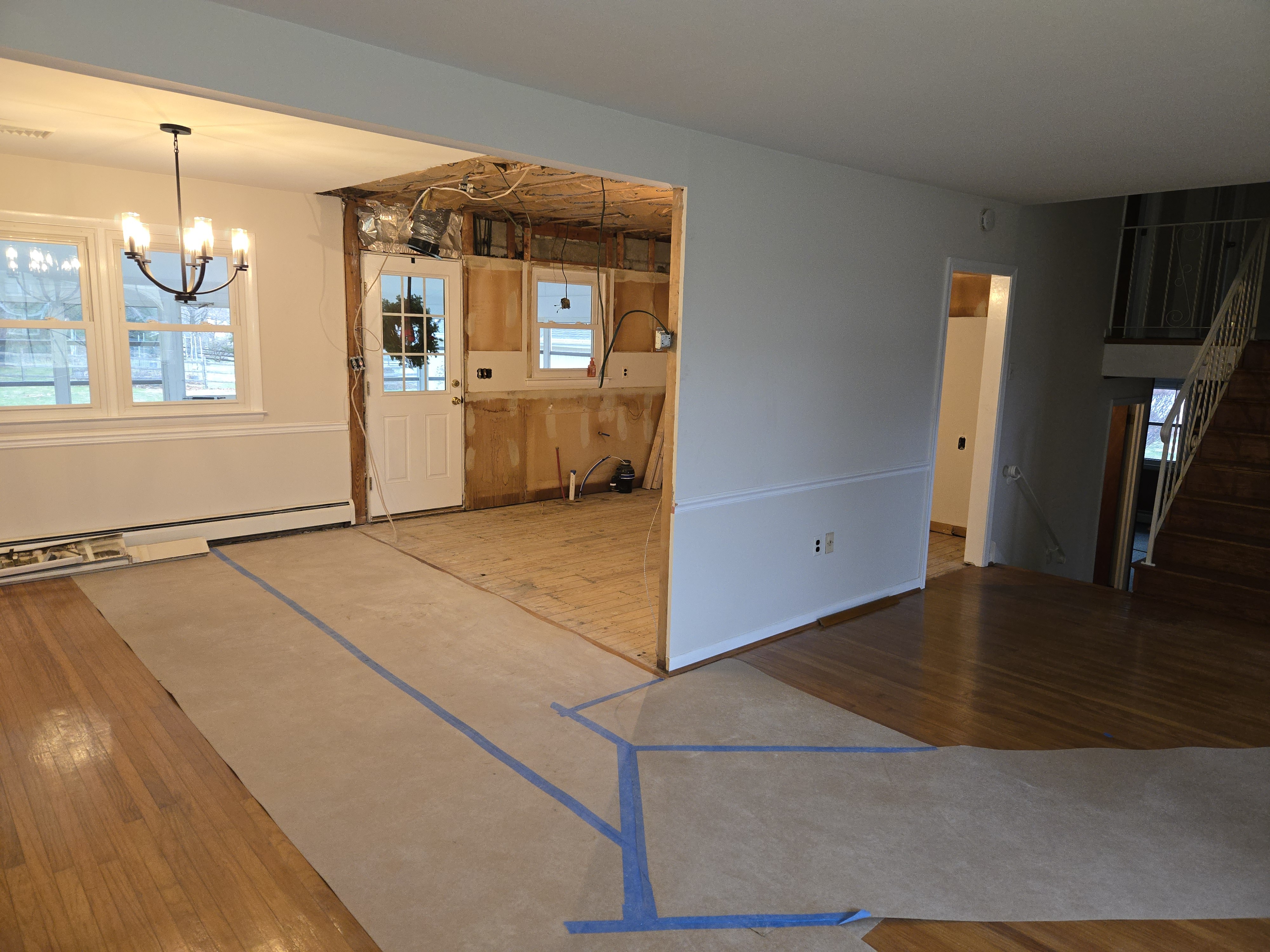 Mid-demo view from the dining room — non-loadbearing wall removed, ram board protecting the existing hardwood floor
