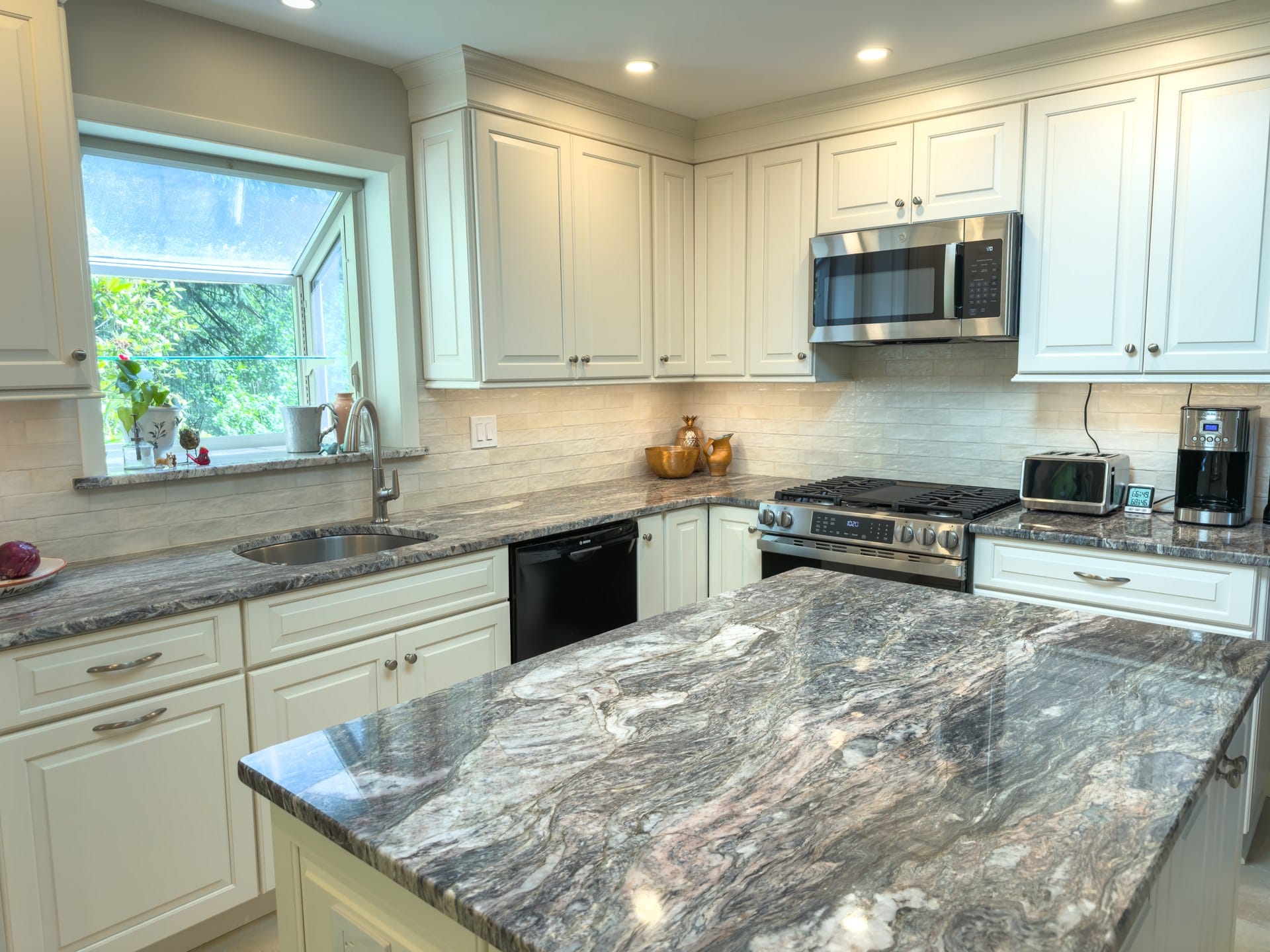 Chester Springs kitchen island in dramatic veined granite with custom cream cabinets, gas range, and tile backsplash