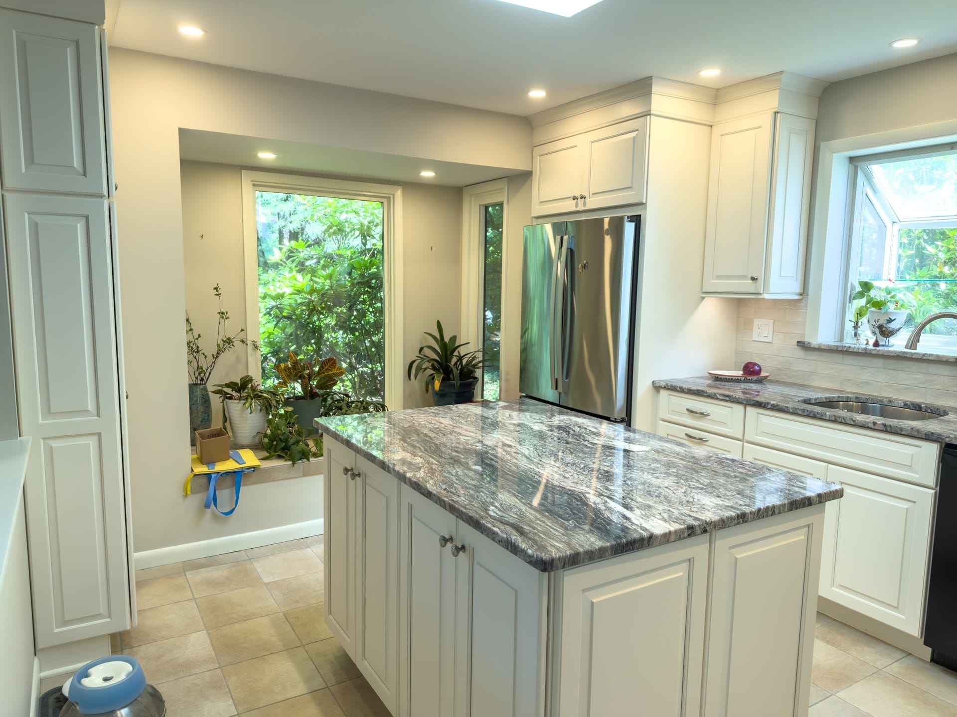 Bright Chester Springs kitchen with cream cabinets, granite island, and garden window overlooking greenery