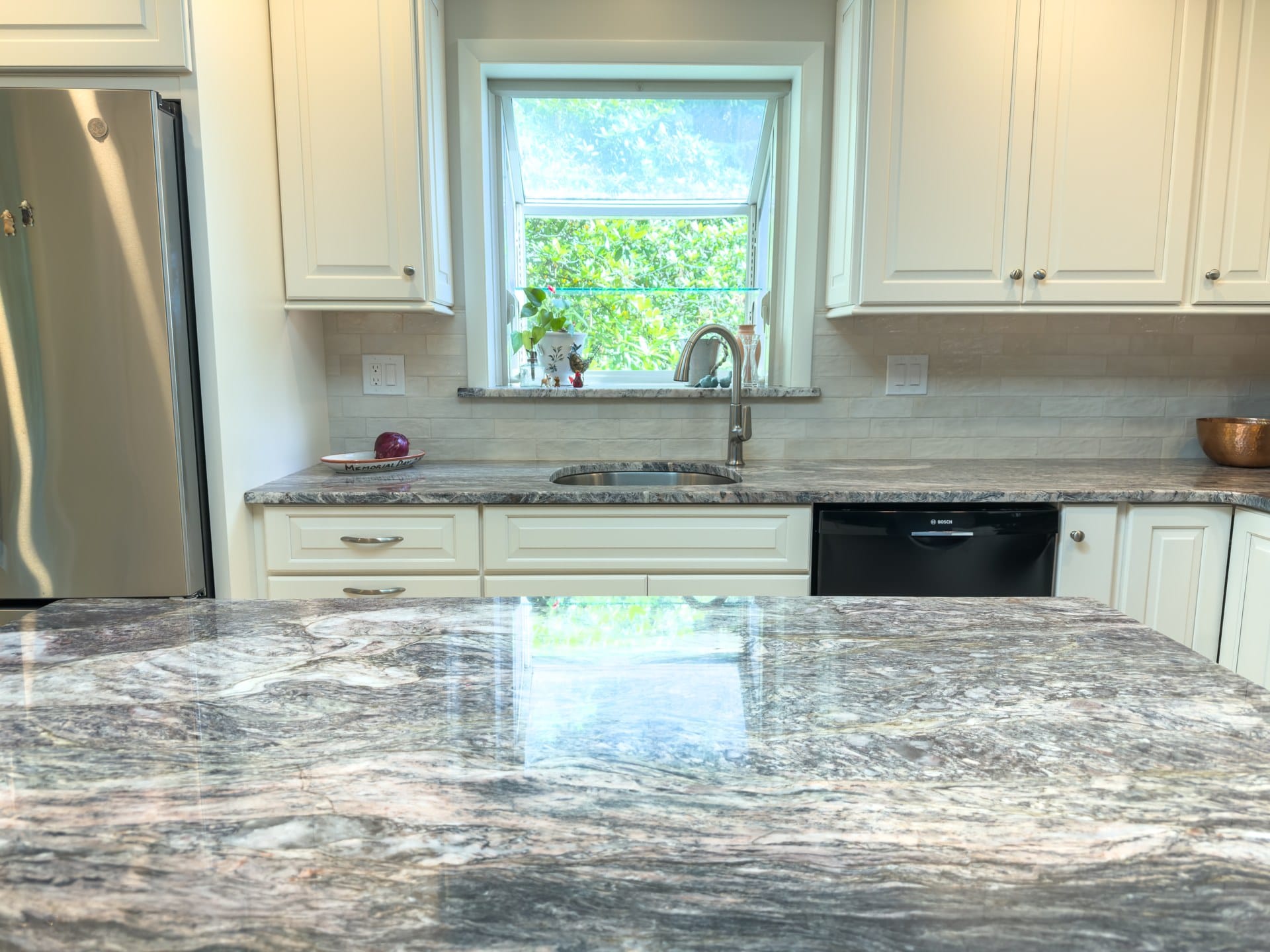 Cream kitchen cabinets, granite counters, and sink under a garden window in Chester Springs