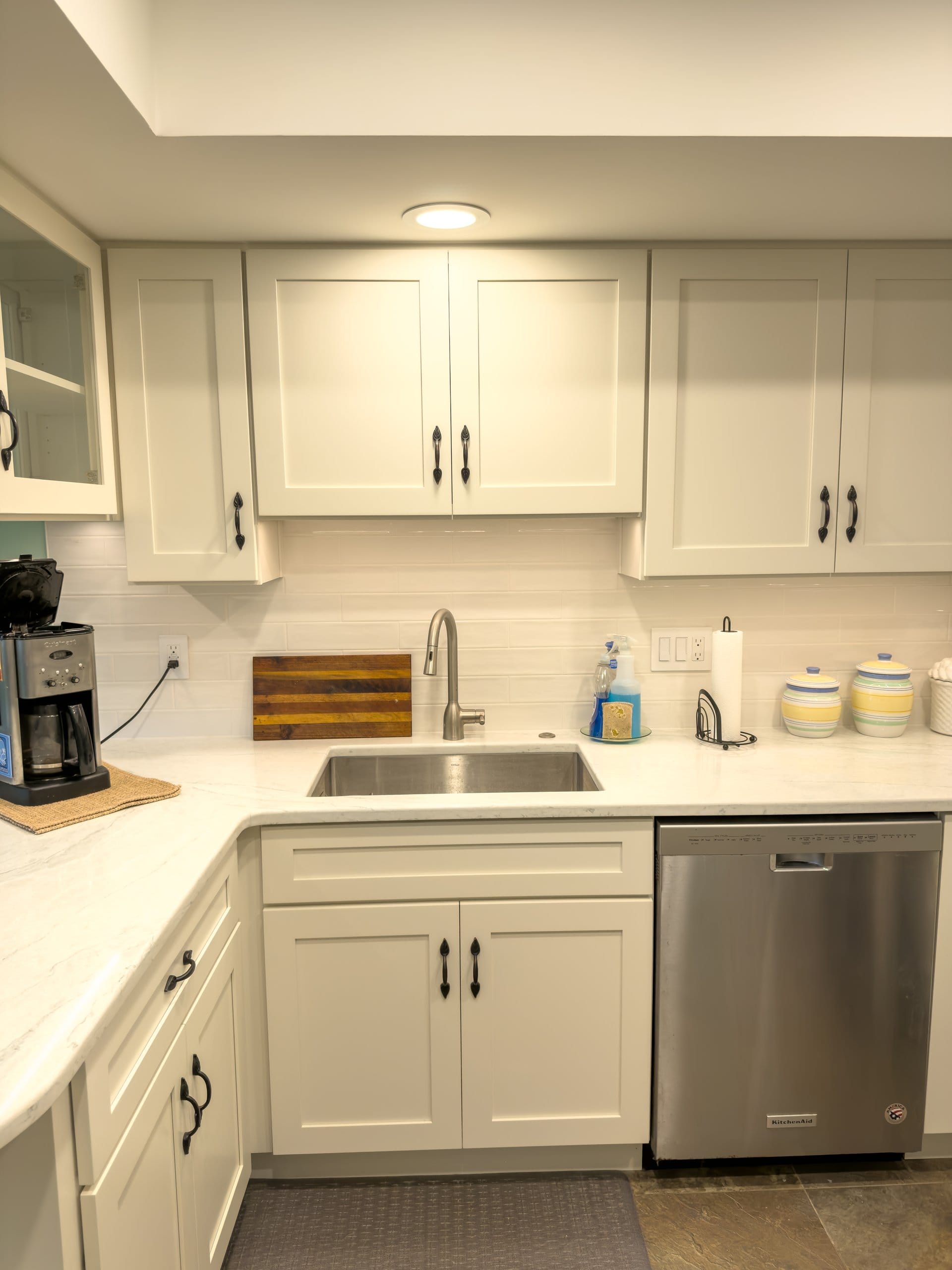 Stainless sink and dishwasher beneath white Shaker cabinets and a subway tile backsplash