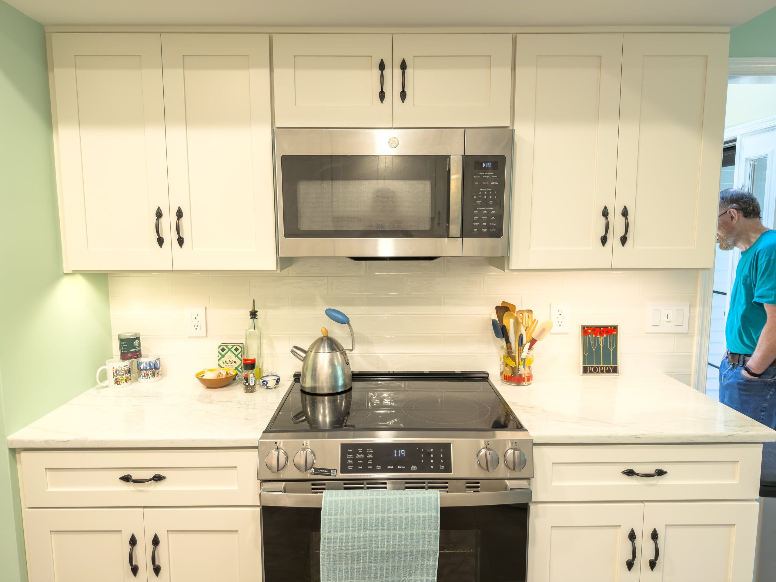 Electric range and stainless microwave framed by white Shaker cabinets