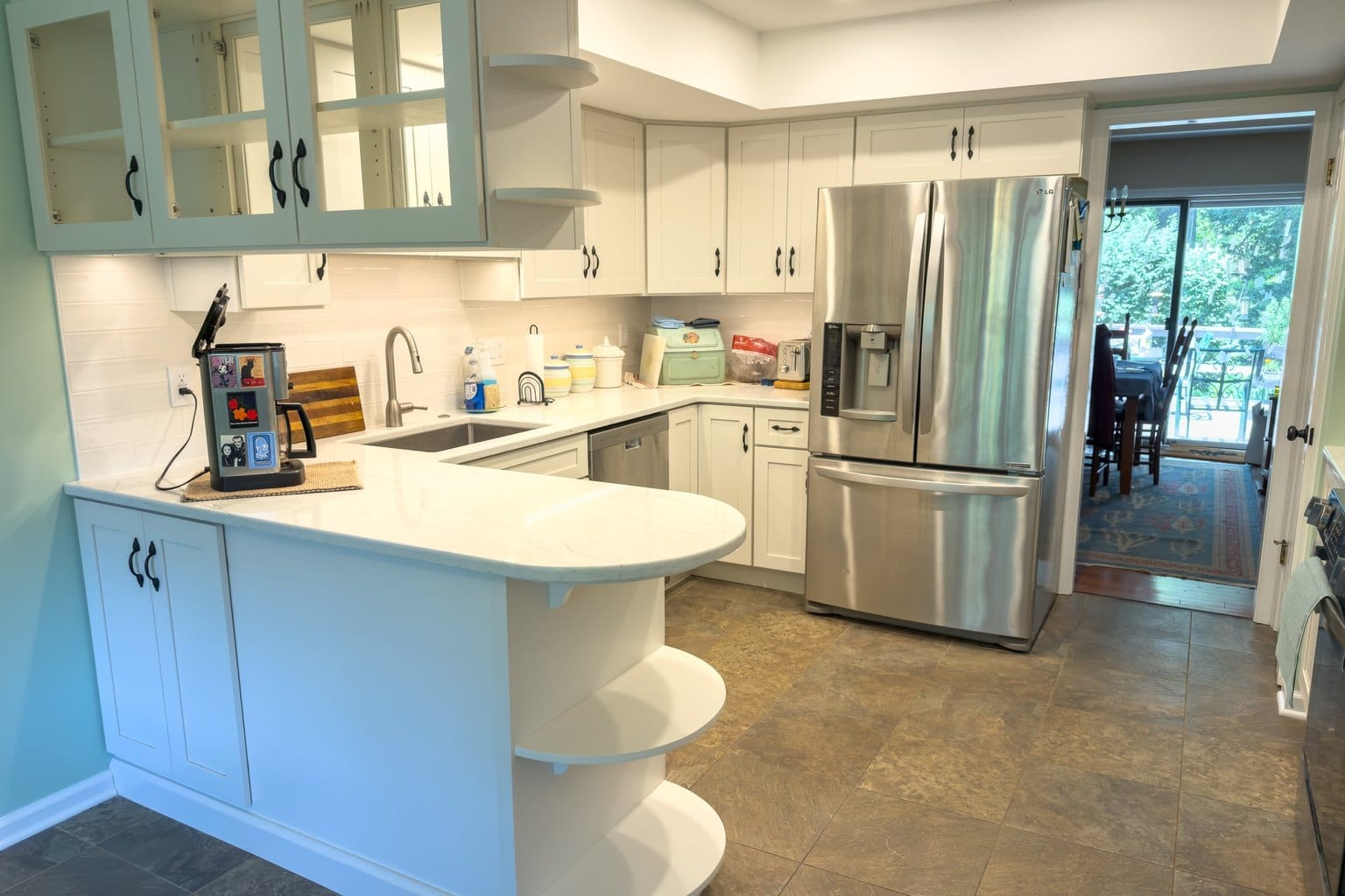 Remodeled West Chester kitchen with a curved white peninsula, glass-front cabinets, and marble-look quartz